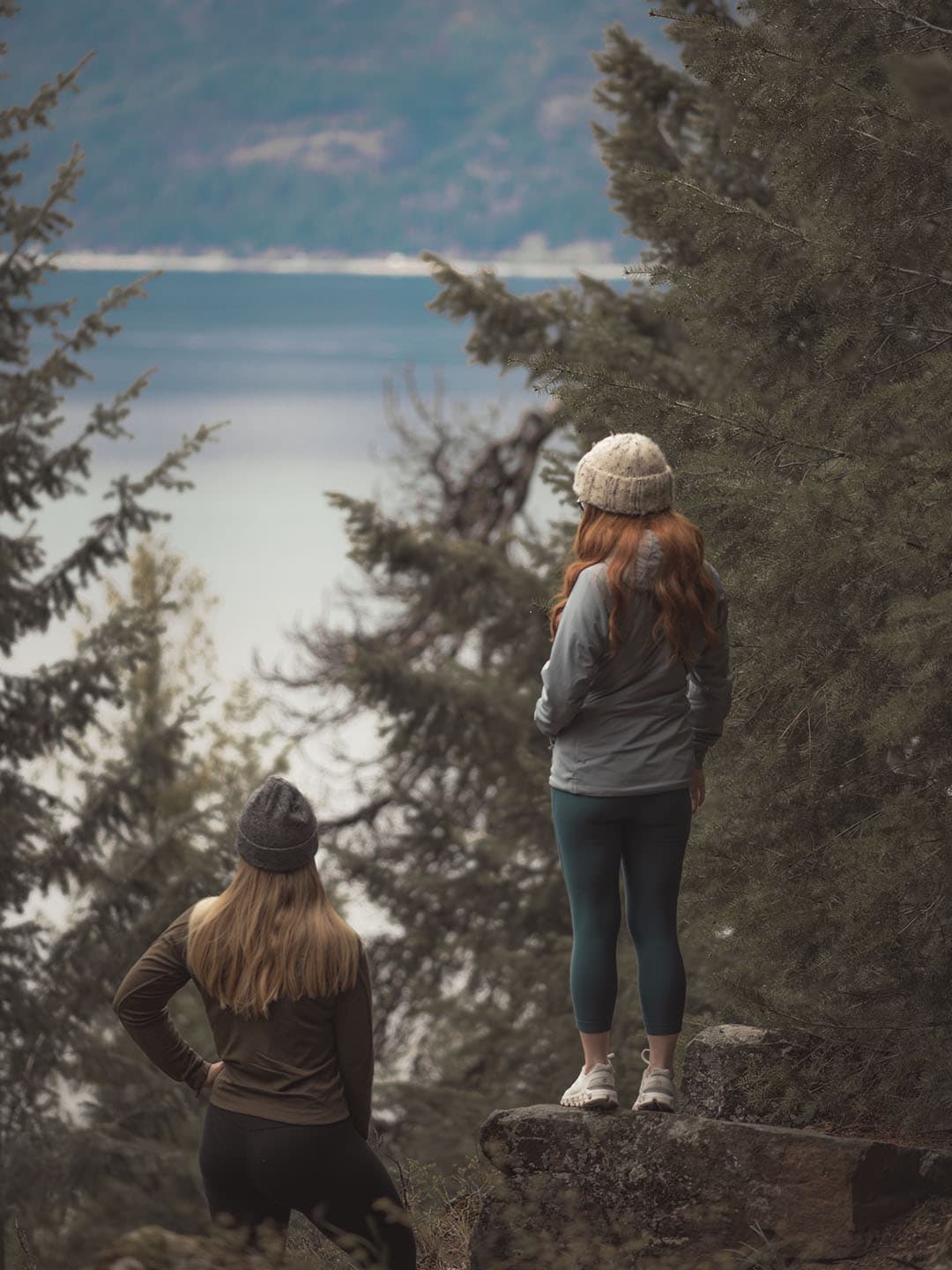 Two hikers looking out over Kootenay Lake from a forested viewpoint.
