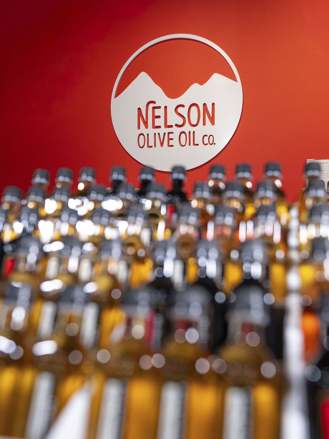 Nelson Olive Oil bottles styled with fresh produce on a kitchen counter.